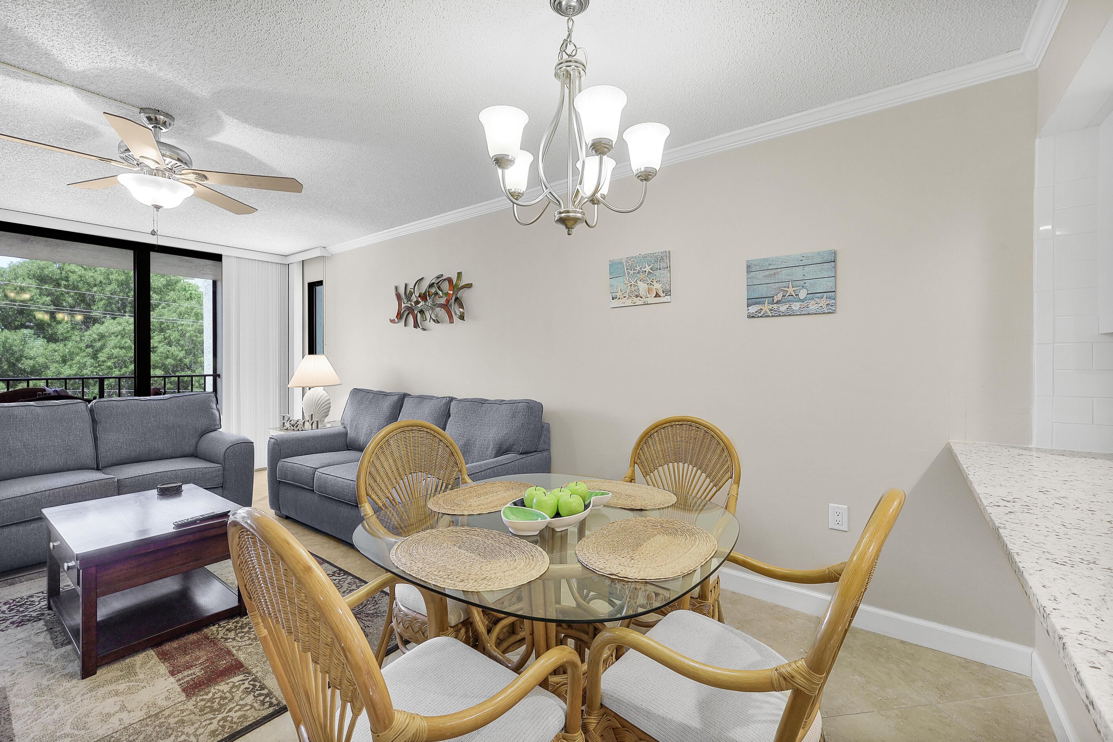 A modern living room with a glass dining table surrounded by wicker chairs, a gray sofa, and a ceiling fan.