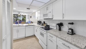A modern kitchen with white cabinetry, a microwave, a stove, and a blender on the countertop. - Stylish Condo Across From South Beach (Marco Island)