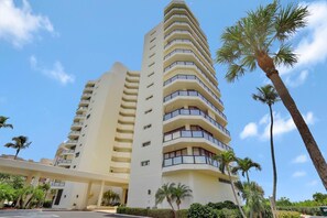 A multi-story hotel with a curved facade, balconies, and palm trees in the foreground. - Sandcastle I-1201 (Marco Island)