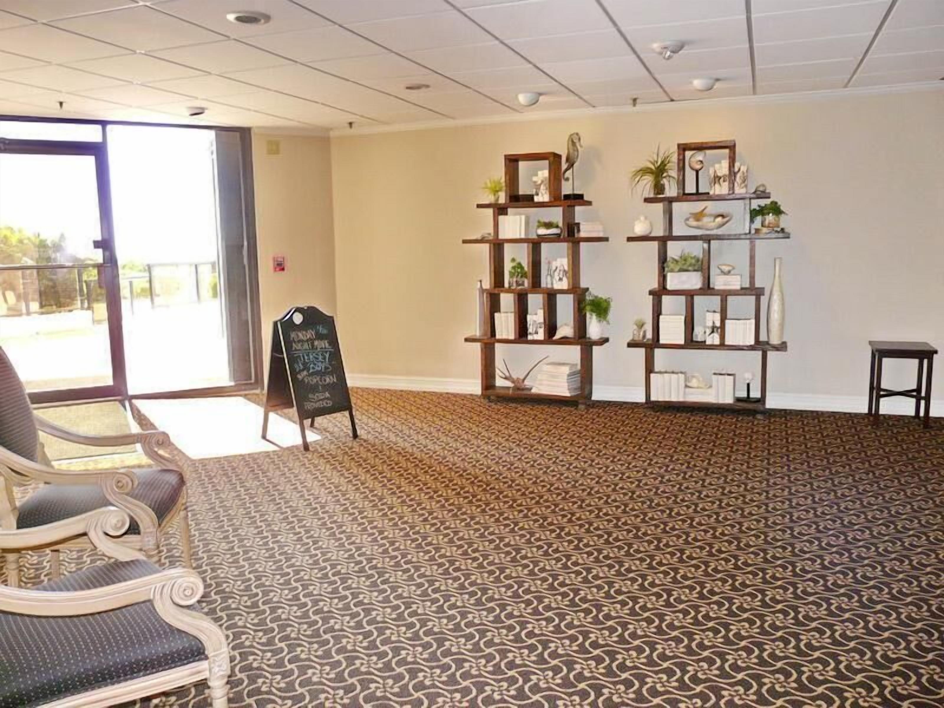 A spacious room with patterned carpet, a large window, and a chair.