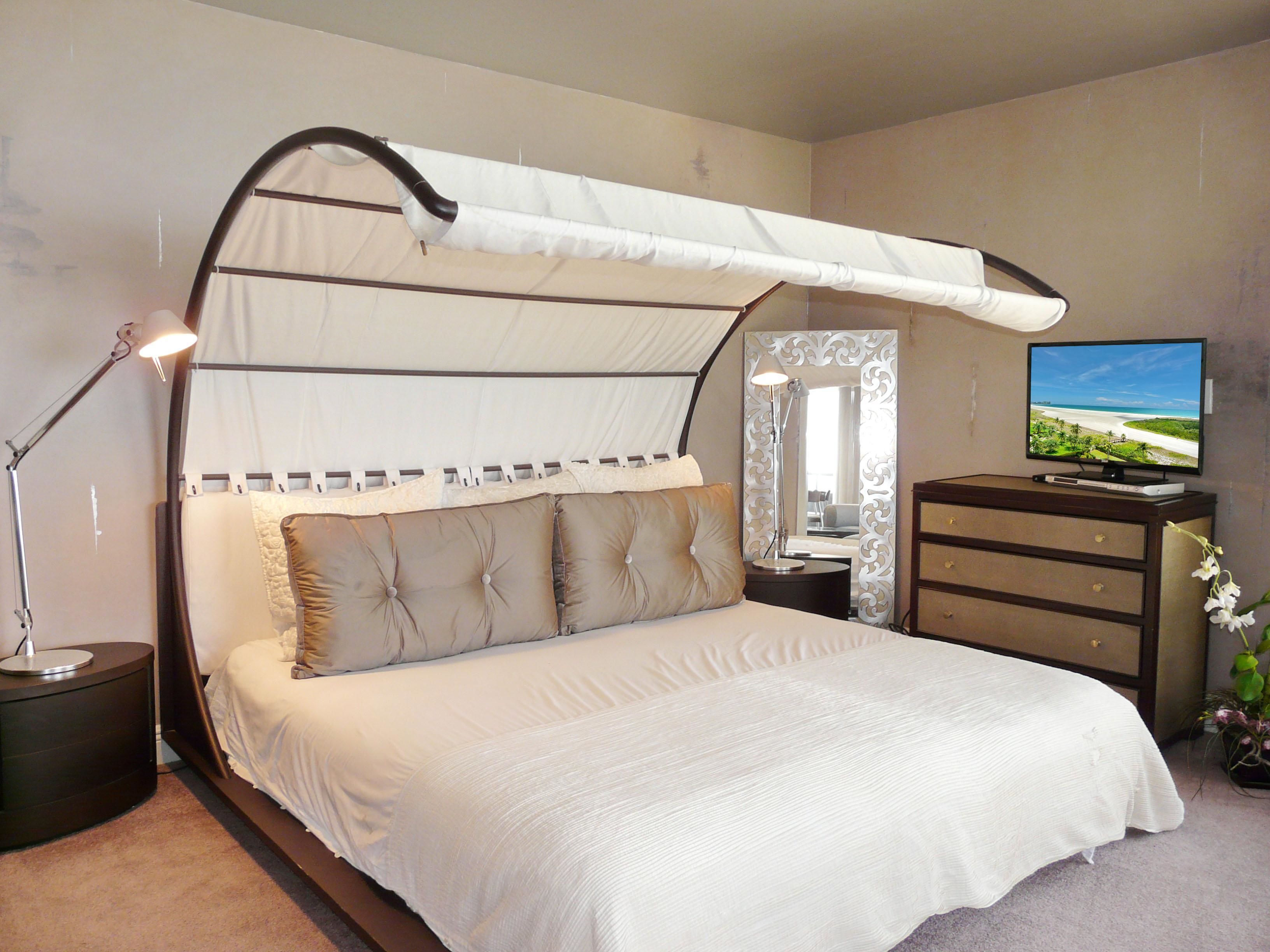 A bedroom with a canopy bed, a television on a dresser, and a mirror on the wall.