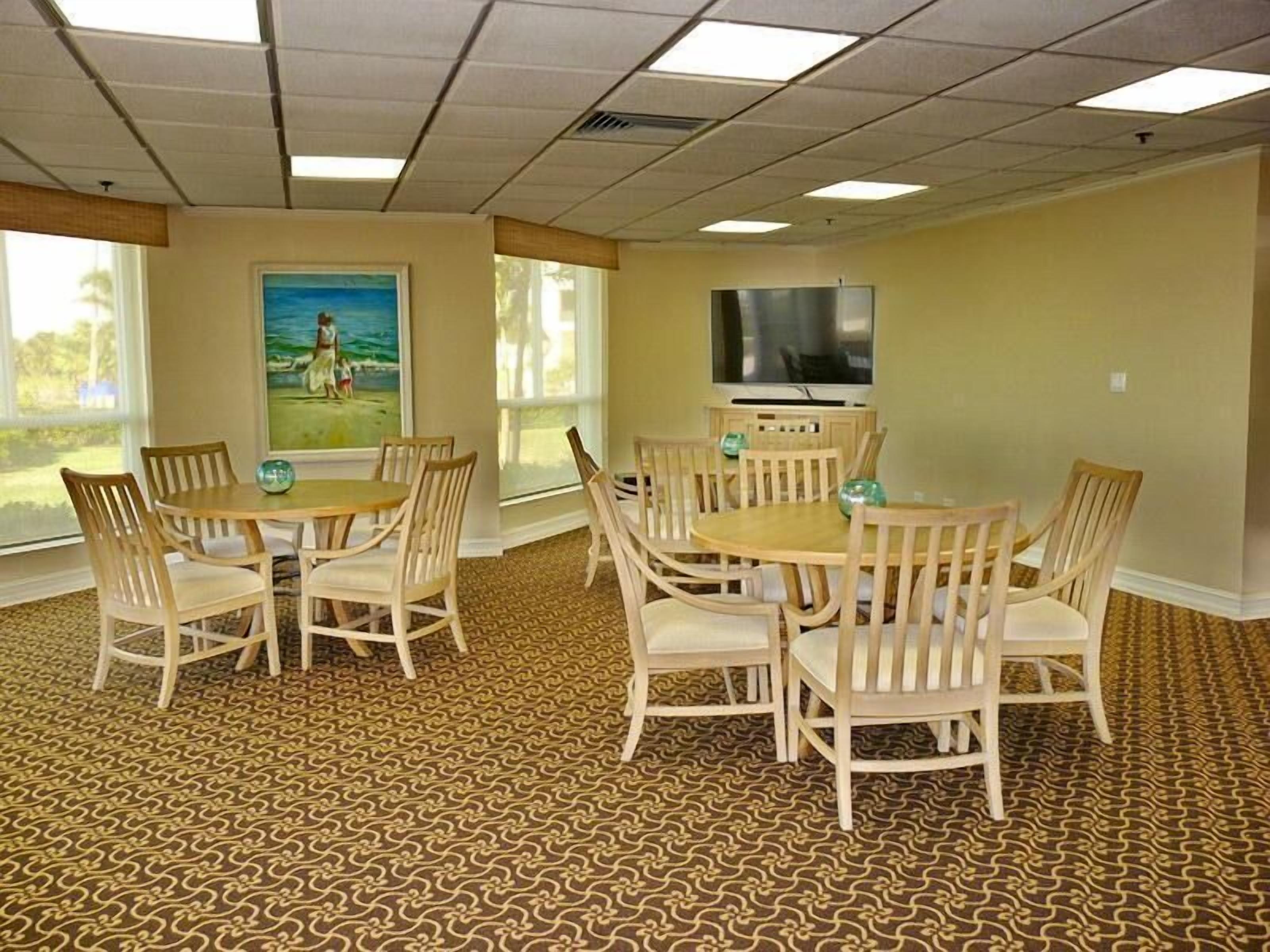 A conference room with a large table and chairs, a painting on the wall, and a television on a stand.