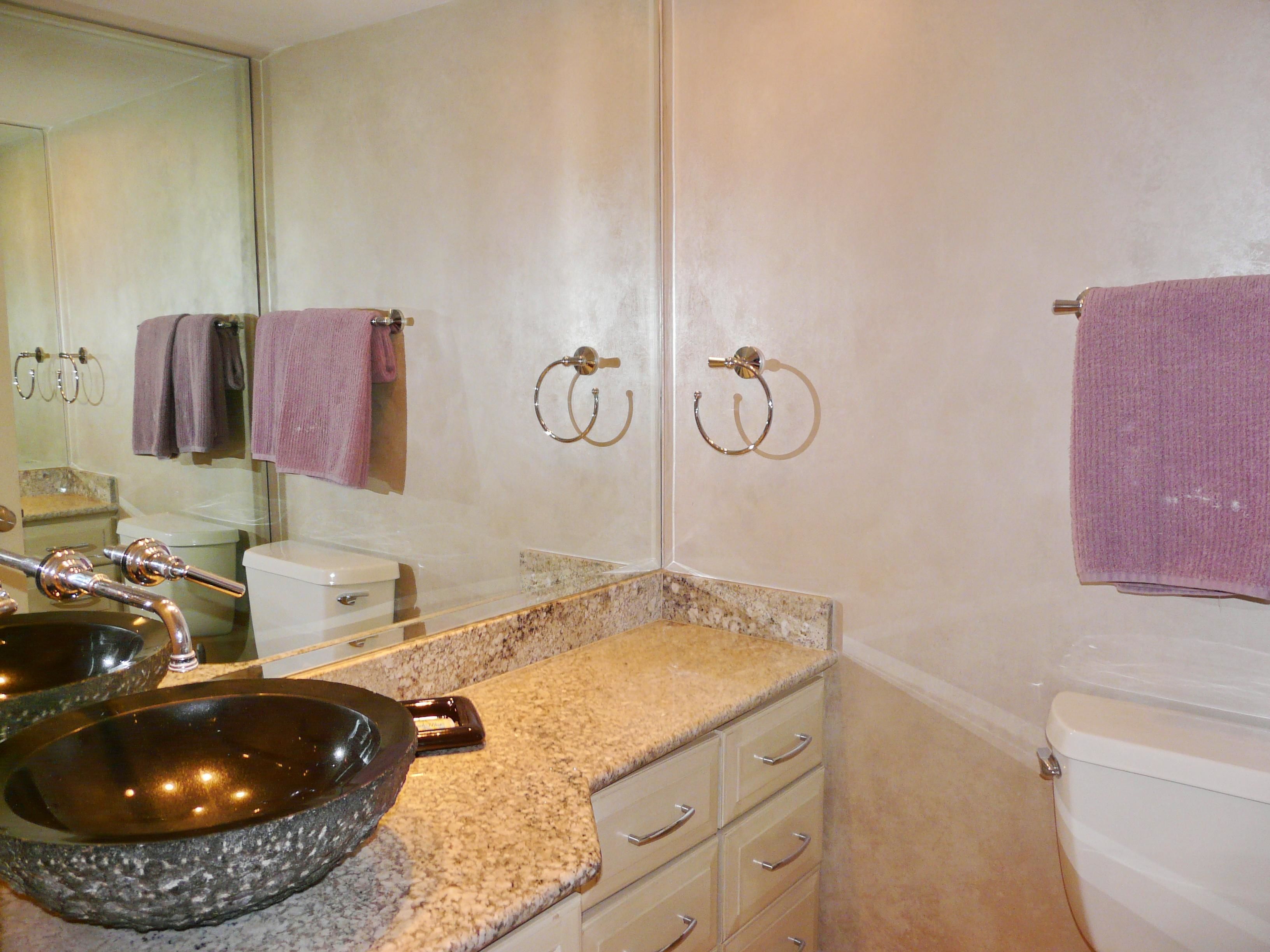 A bathroom with a granite countertop, a vessel sink, a toilet, and a mirror.