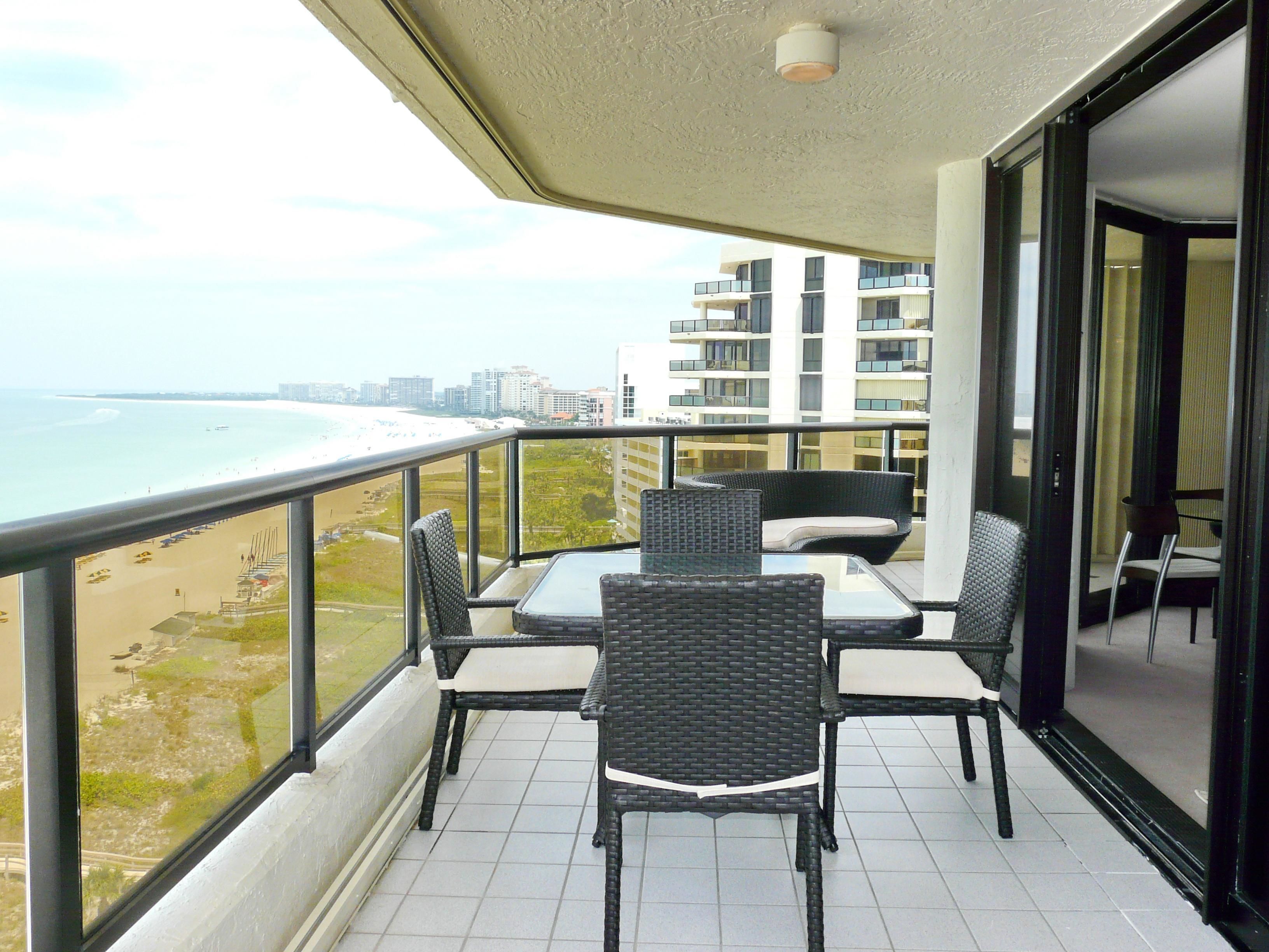 A balcony with a table and chairs, overlooking a beach and cityscape.