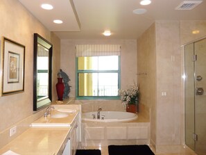 A bathroom with two sinks, a bathtub, a window with curtains, a shower, and a mirror. - Cozumel 2205 (Marco Island)