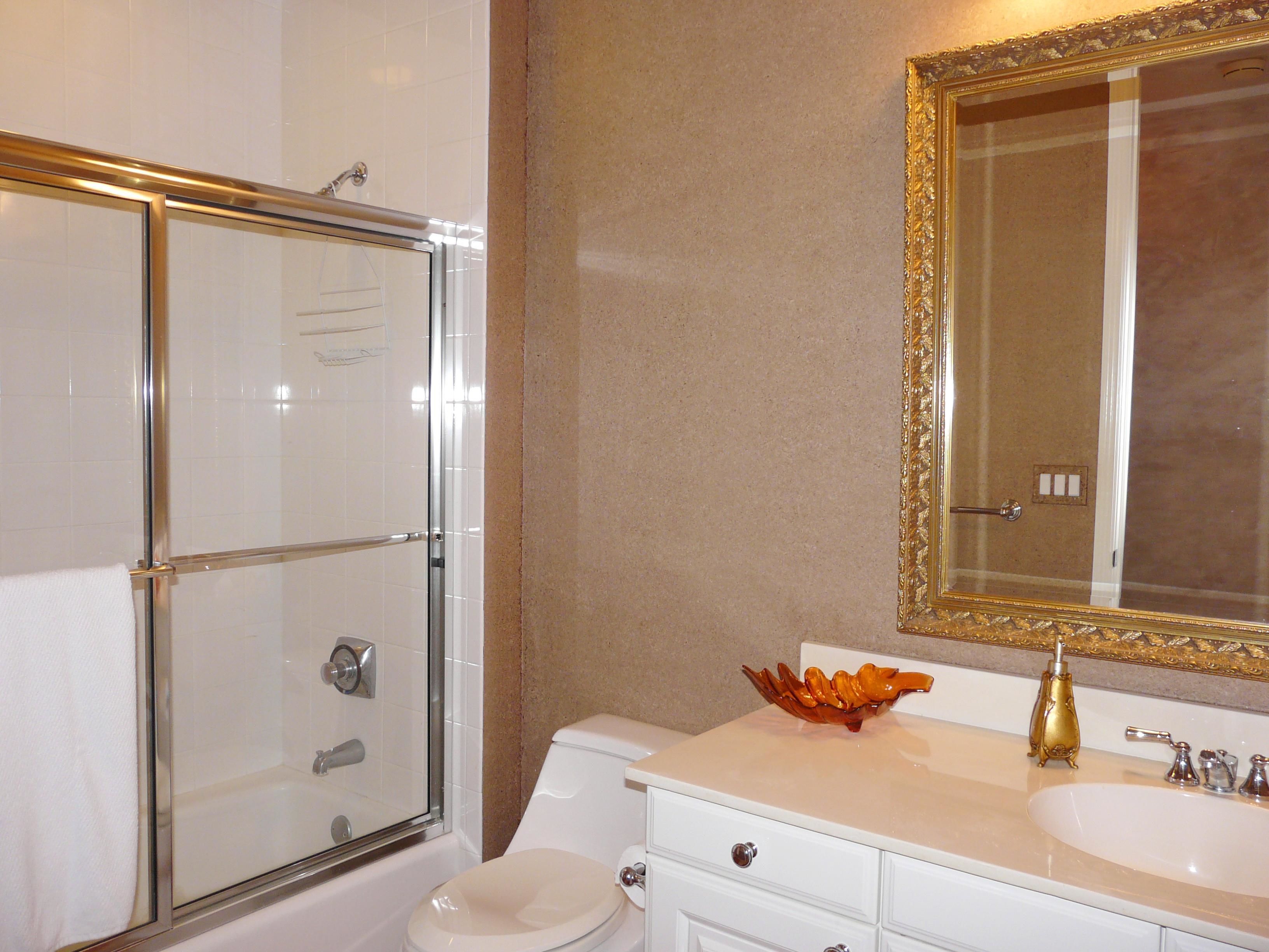 A bathroom with a glass shower enclosure, a toilet, a sink with a gold faucet, and a decorative bowl on the counter.