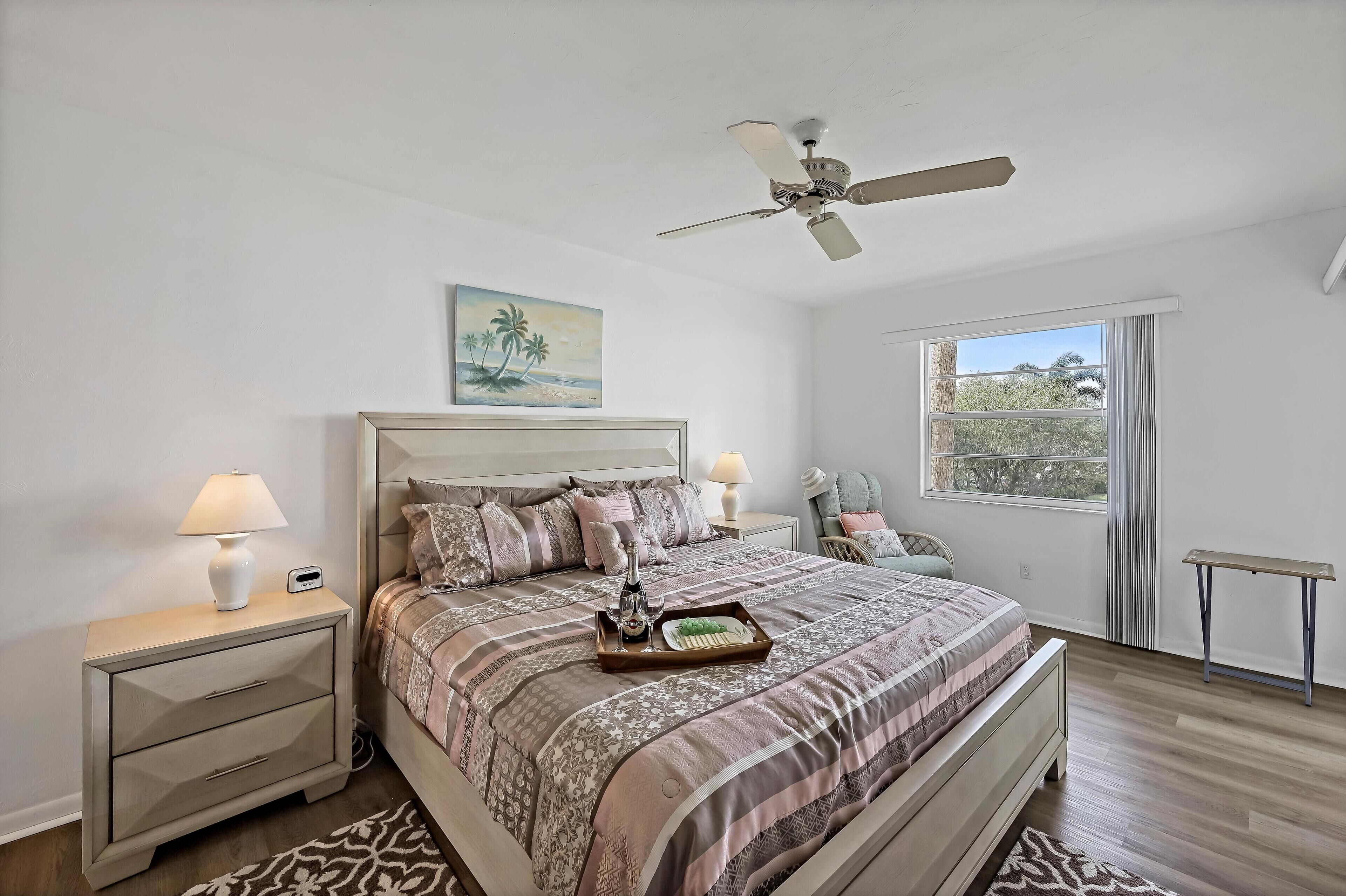 Une chambre à coucher avec un lit, des tables de chevet, un ventilateur de plafond, une fenêtre et un tableau.