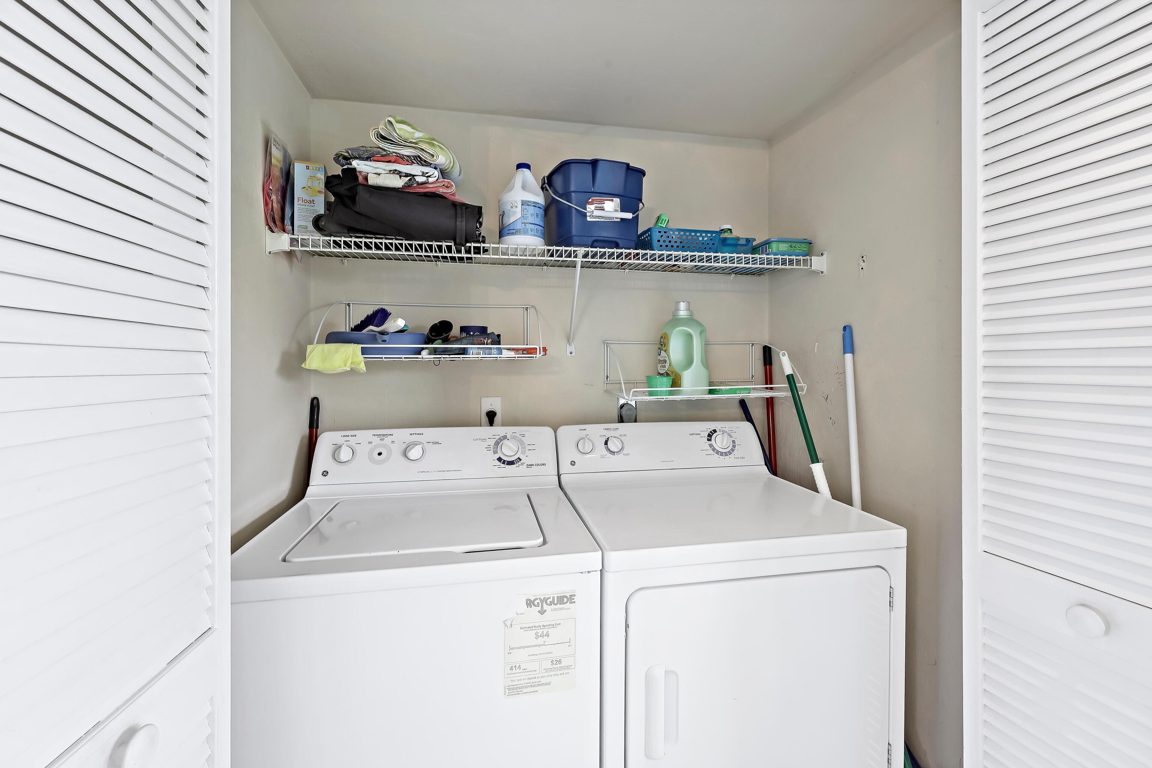 A laundry room with two washing machines, shelves with folded clothes and laundry supplies, and a mop on the right.