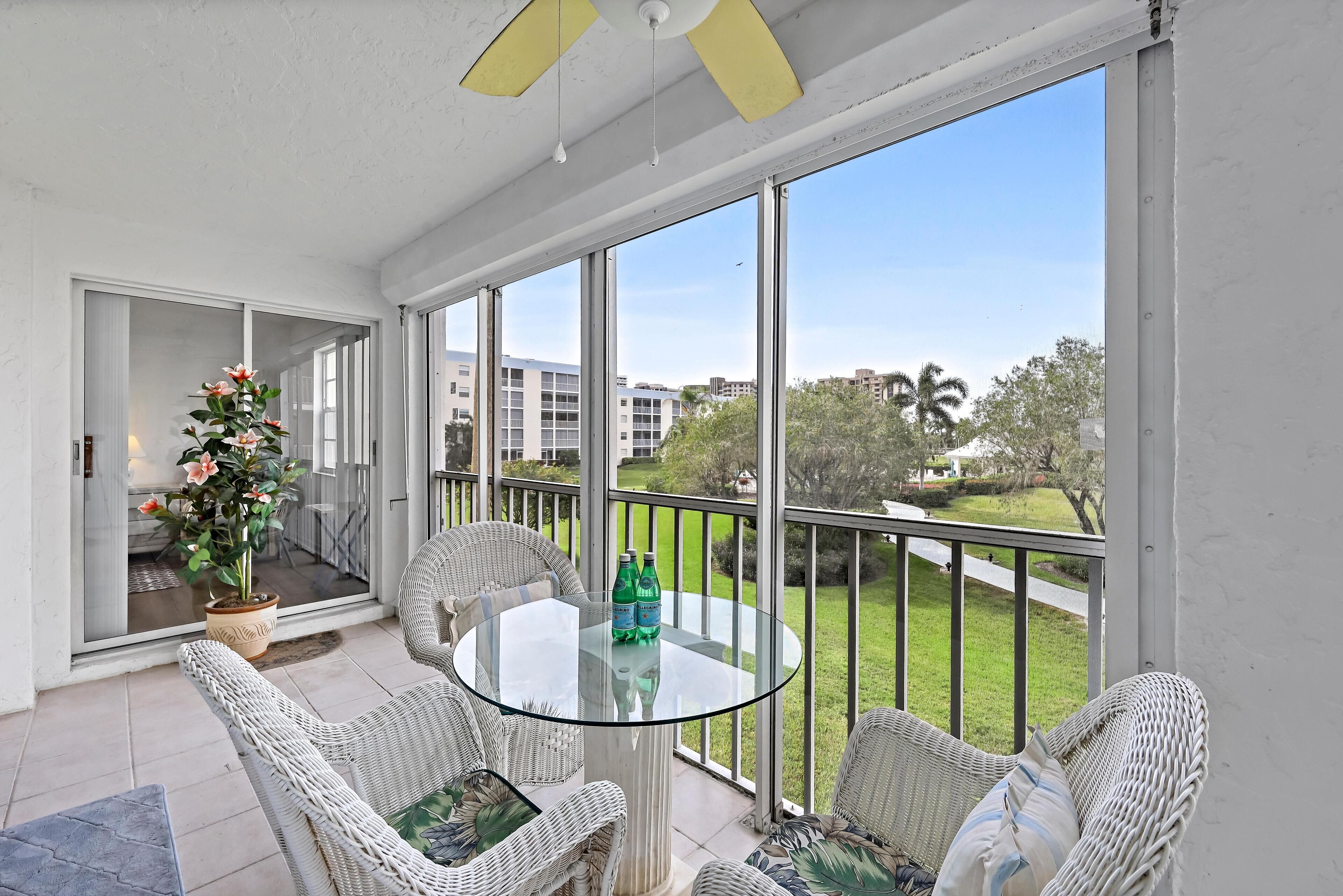 A balcony with wicker furniture, a glass table, and a potted plant.