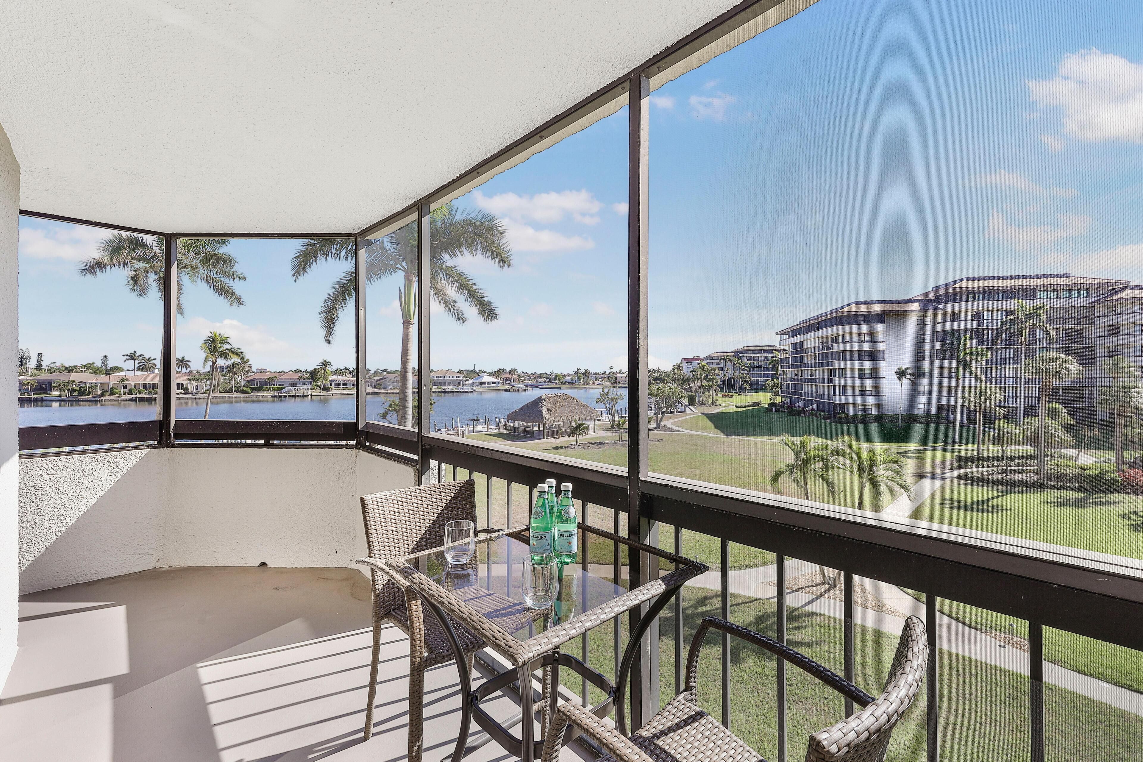 A balcony with a glass table, wicker chairs, and a view of a golf course and buildings.