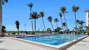 A rectangular swimming pool with a tiled deck, surrounded by lounge chairs and palm trees.
