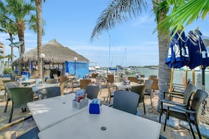 Guests can dine al fresco under shaded umbrellas surrounded by palm trees and a thatched-roof bar.