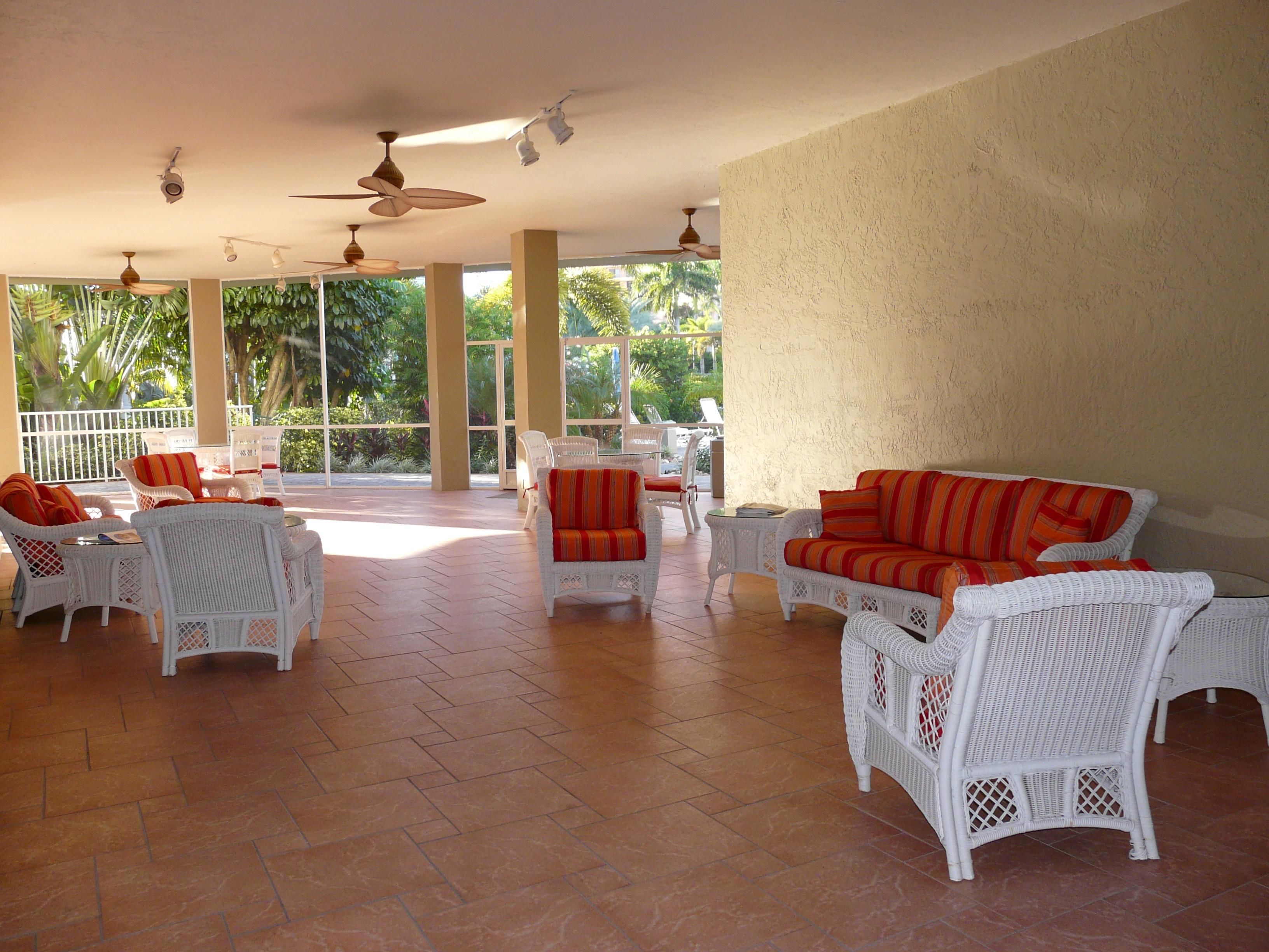 An open-plan living area with wicker furniture, large windows, and ceiling fans.