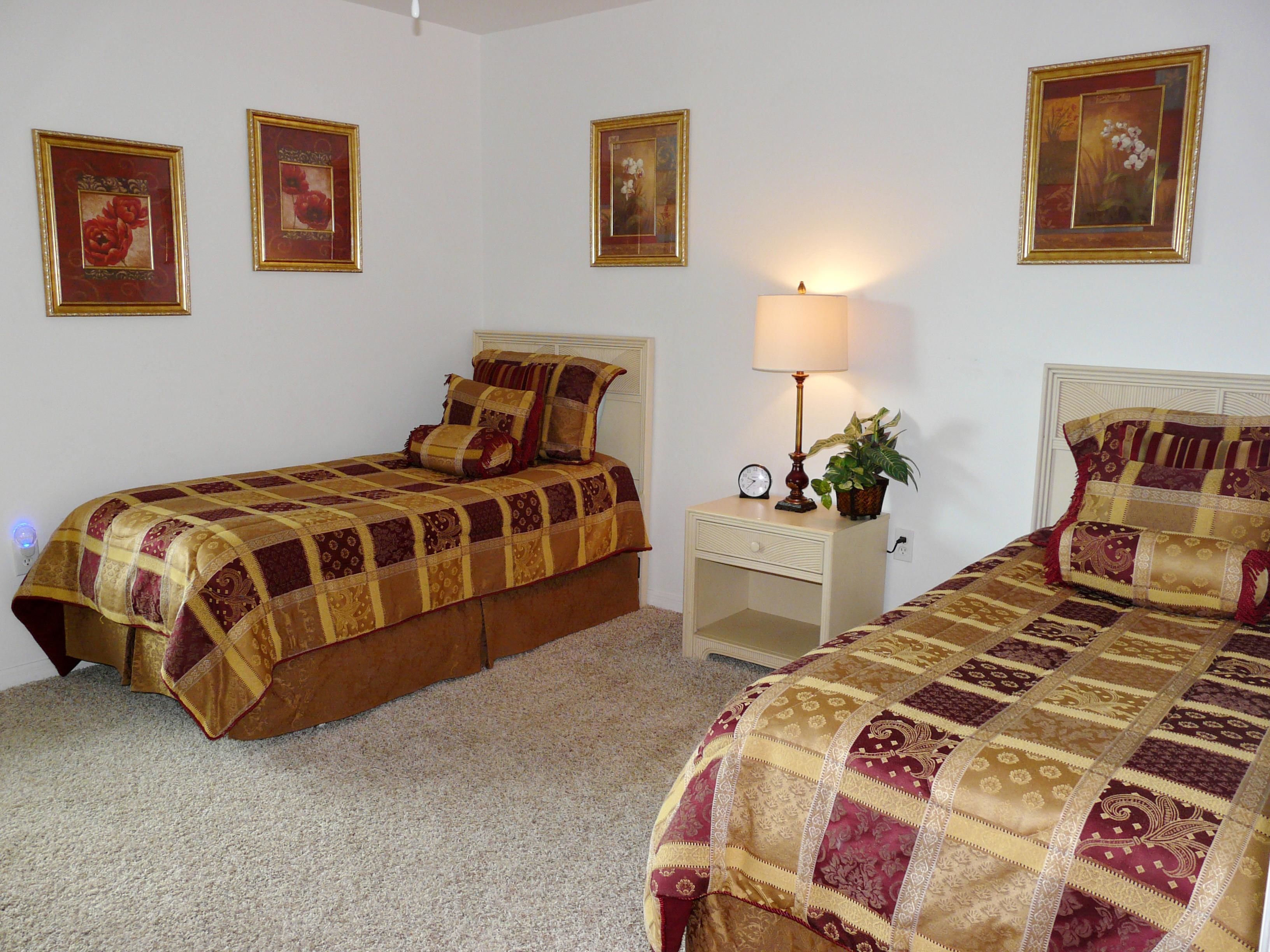 A bedroom with two beds, a nightstand with a lamp, a clock, and a potted plant.