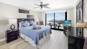 Ein Schlafzimmer mit Bett, Nachttischen, Deckenventilator, Fernseher und einem Balkon mit Blick.