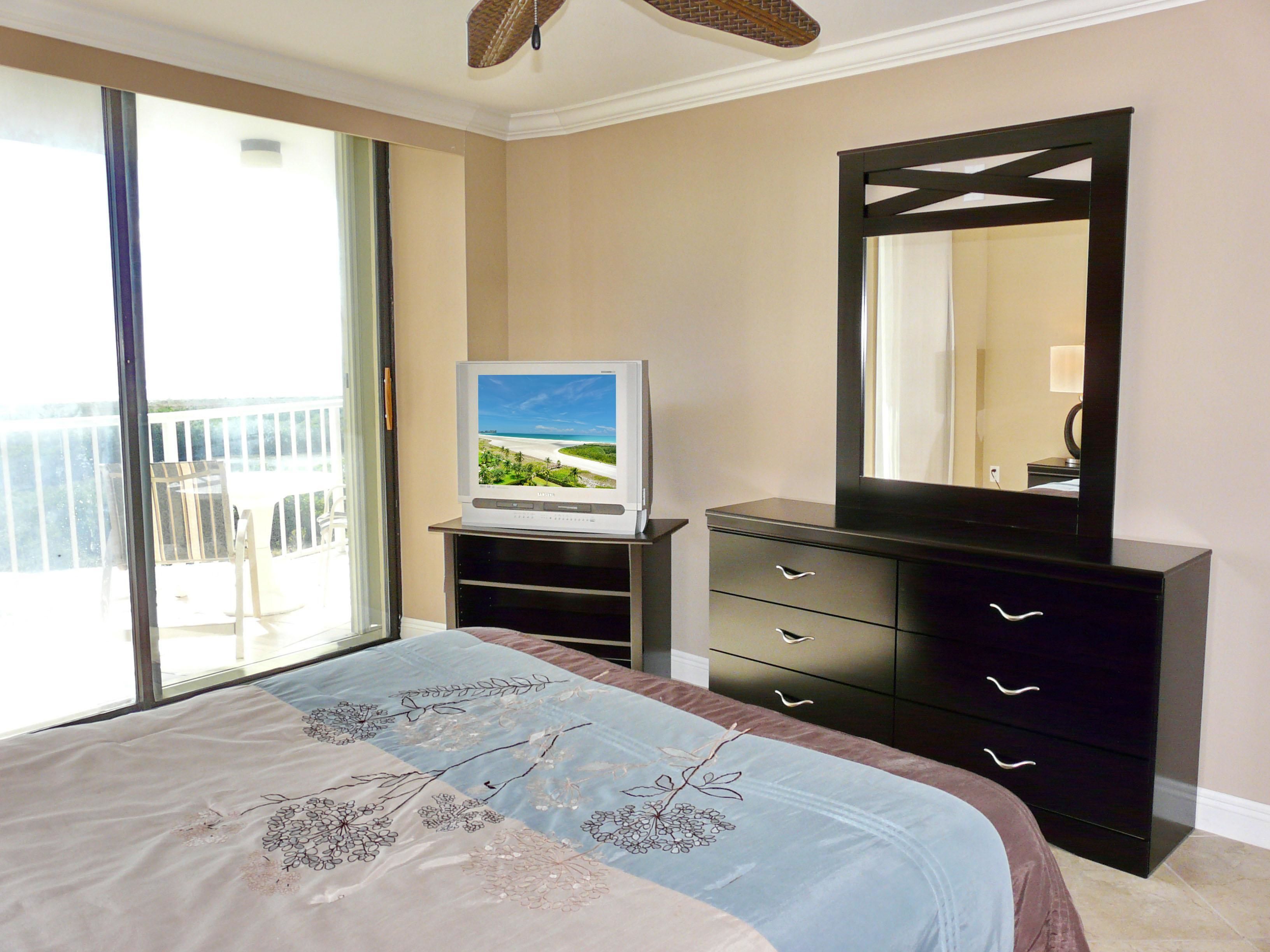 A bedroom with a bed, a television on a stand, a dresser, and a balcony with a view.