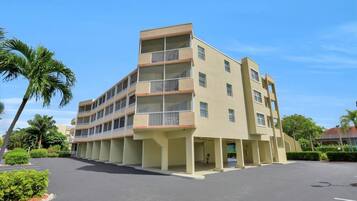 Un edificio de varios pisos con balcones, un estacionamiento y palmeras.