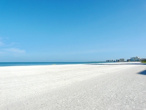 Uma extensa praia arenosa, com céu azul límpido e mar calmo.