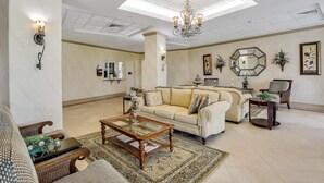 A spacious living room with a large sofa, a coffee table, and a chandelier. - Cozy Beachfront Condo With Pool and Tennis Courts (Marco Island)