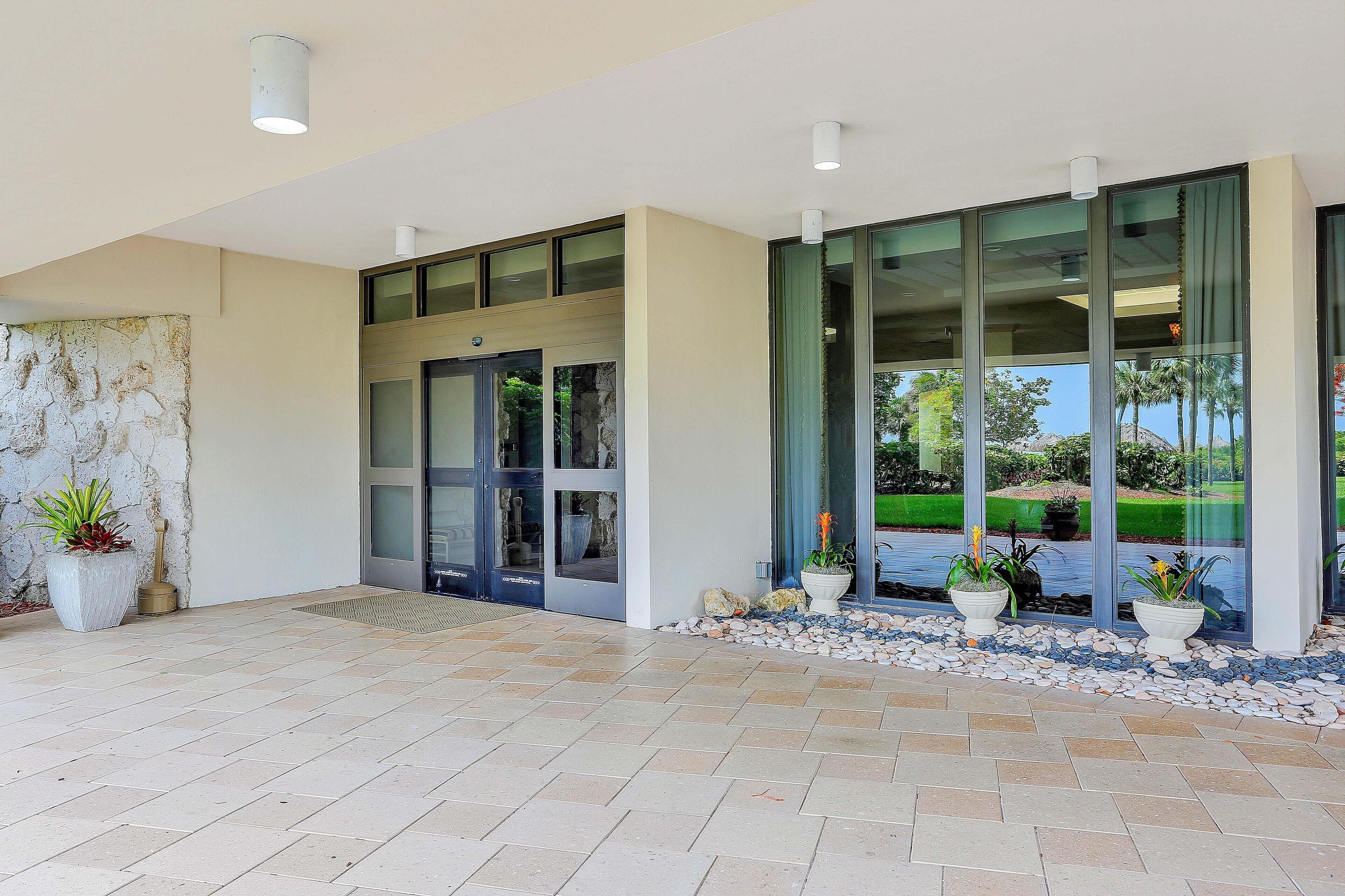 A modern building entrance with glass doors, potted plants, and a tiled floor.