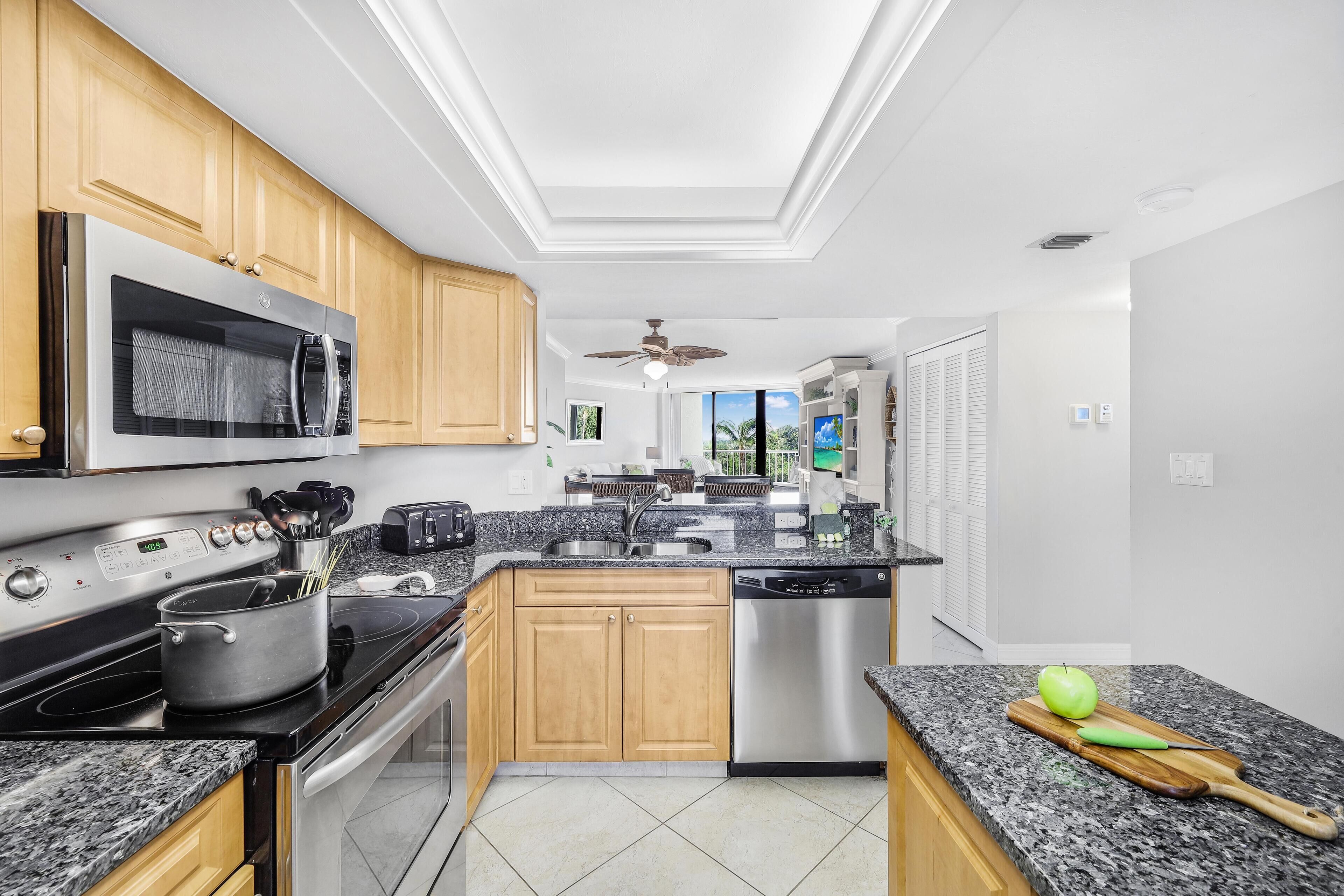 A modern kitchen with granite countertops, stainless steel appliances, wooden cabinets, and a view to the outside.