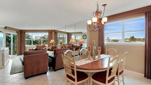 A spacious living room with a dining area, large windows, and a chandelier.