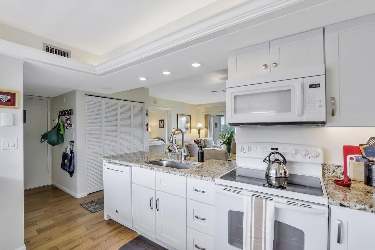 A modern kitchen with white cabinets, a granite countertop, a microwave, and a kettle.
