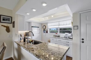 A modern kitchen with granite countertops, white cabinetry, and a built-in oven. - Island-style Condo With Pool, spa and Steps to Beach (Marco Island)