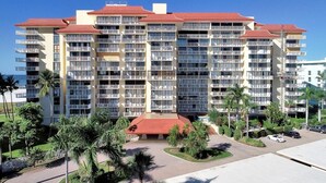A multi-story hotel with balconies, a red roof, and a landscaped front yard with palm trees. - Inviting Beachfront Condo With Large Balcony and Pool (Marco Island)