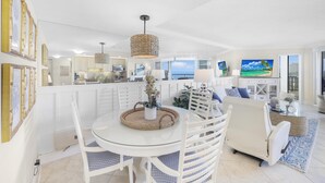 A spacious living area with a dining table, white furniture, and a large TV. - Cozy Beachfront Getaway With Pool and spa (Marco Island)