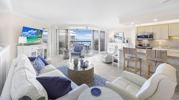 A spacious living area with a large flat-screen TV, comfortable seating, a kitchen with modern appliances, and a view of the ocean. - Cozy Beachfront Getaway With Pool and spa (Marco Island)