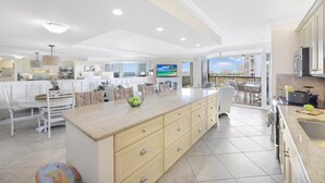 A spacious kitchen with a large island, white cabinetry, and a view to the outside. - Cozy Beachfront Getaway With Pool and spa (Marco Island)