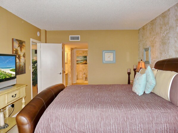 Un dormitorio con una cama grande, televisión y un baño visible a través de una puerta abierta.