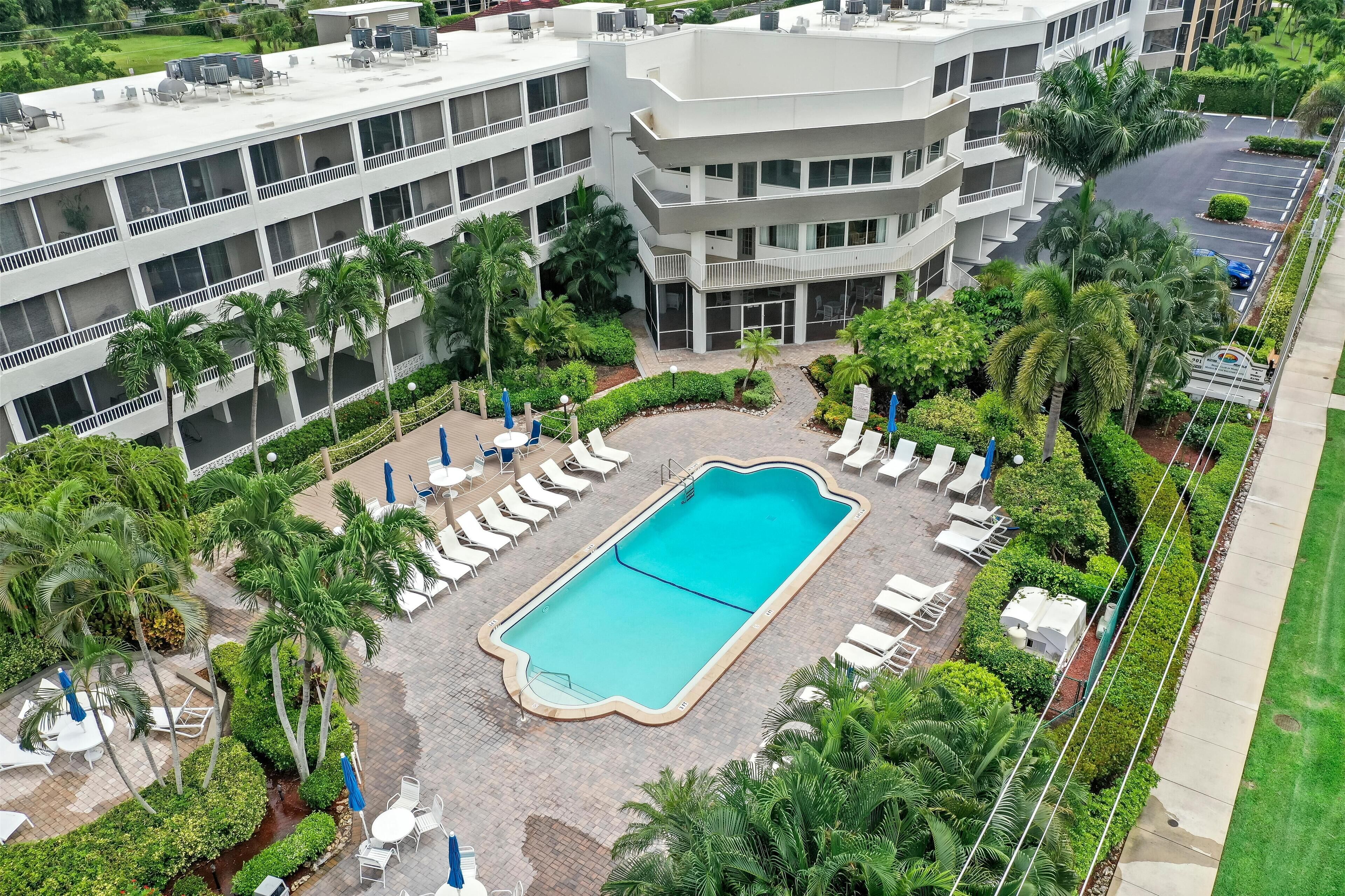 A multi-story hotel with a swimming pool surrounded by palm trees and lounge chairs.