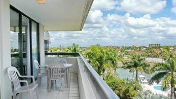 A balcony with two white plastic chairs and a small table, overlooking a pool and palm trees.
