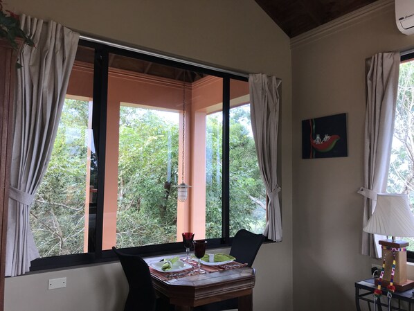 Un comedor con una mesa dispuesta para dos, una silla, una lámpara y un ventanal con cortinas.