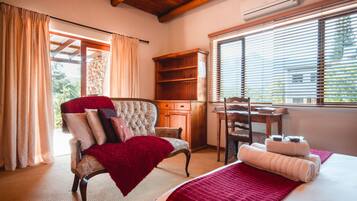 A bedroom with a bed, a chair, a desk, and a window with blinds.