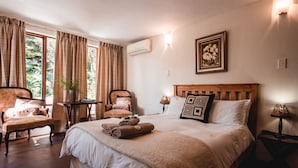 A bedroom with a large bed, two chairs, a small table, and a wall-mounted air conditioner. - Wildebraam Berry Estate (Swellendam)