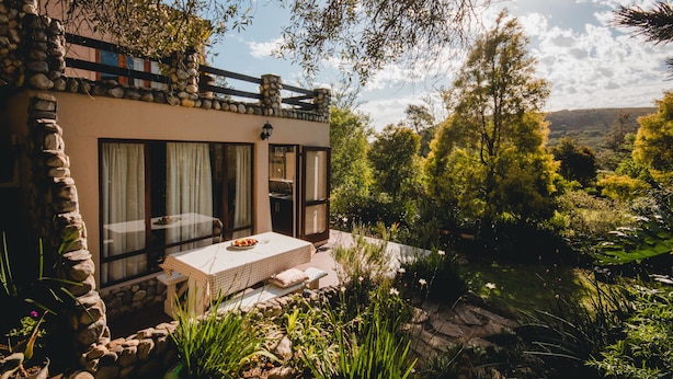 A modern house with a stone facade, large windows, and a patio with a table and chairs. - Wildebraam Berry Estate (Swellendam)