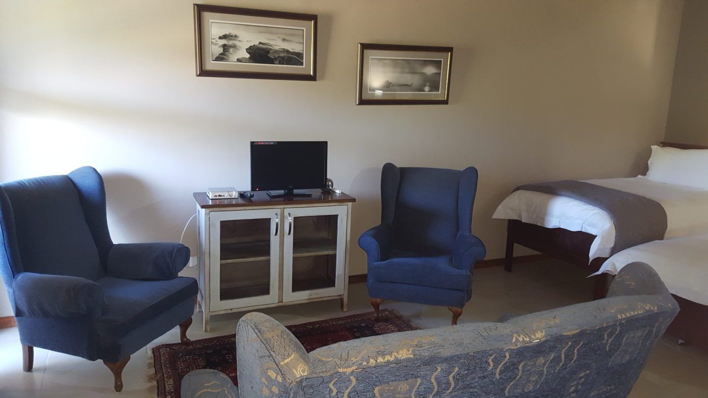 Habitación de hotel con dos sillones azules, un mueble bajo con televisor y una cama con ropa de cama blanca.