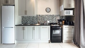 A kitchen with white cabinets, a black stove, a microwave, and a tiled backsplash. - Wildebraam Berry Estate (Swellendam)