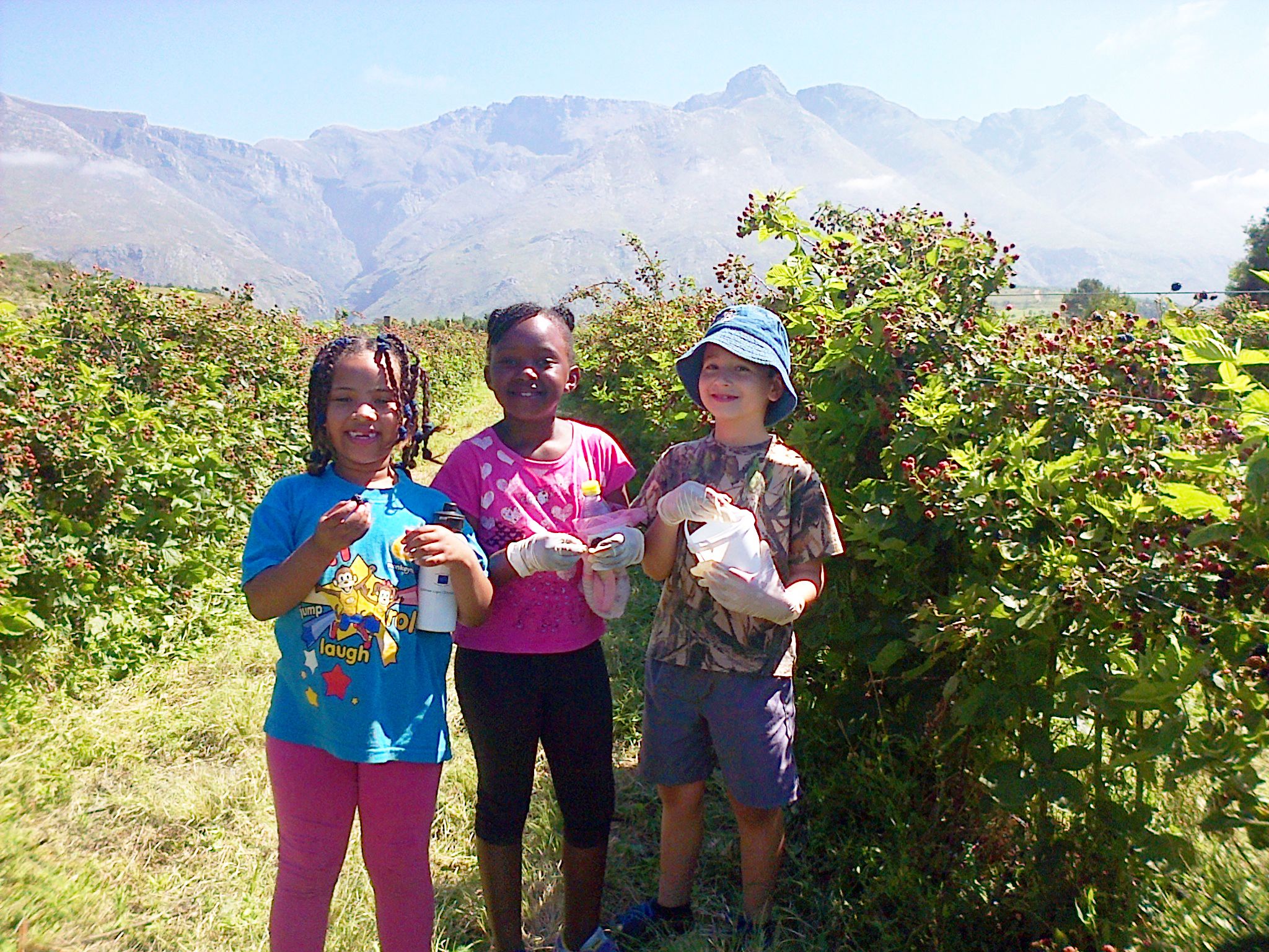 Three people standing in a natural setting with mountains in the background.