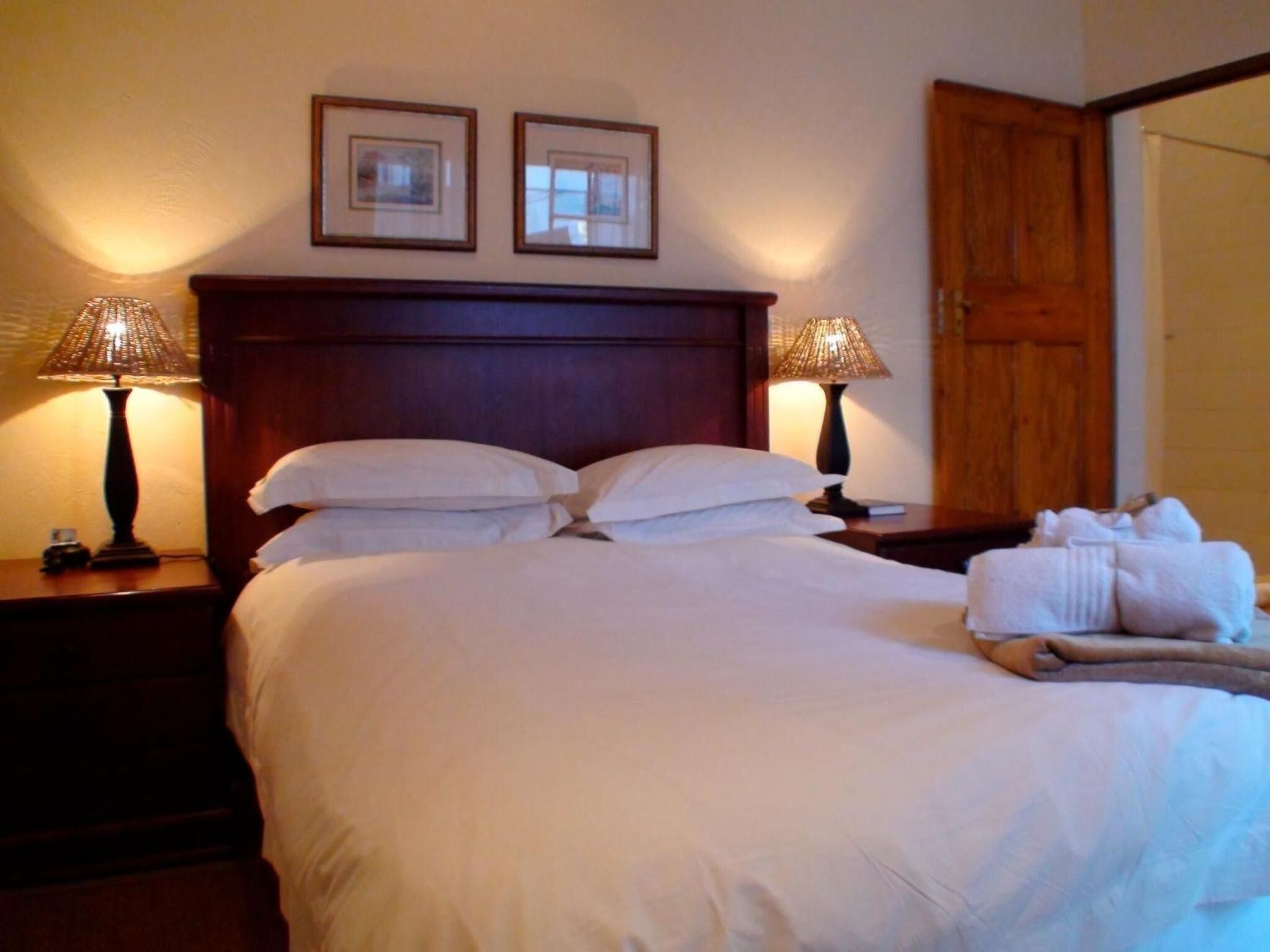 A neatly made bed with white linens, two bedside lamps, and a set of towels on the side.