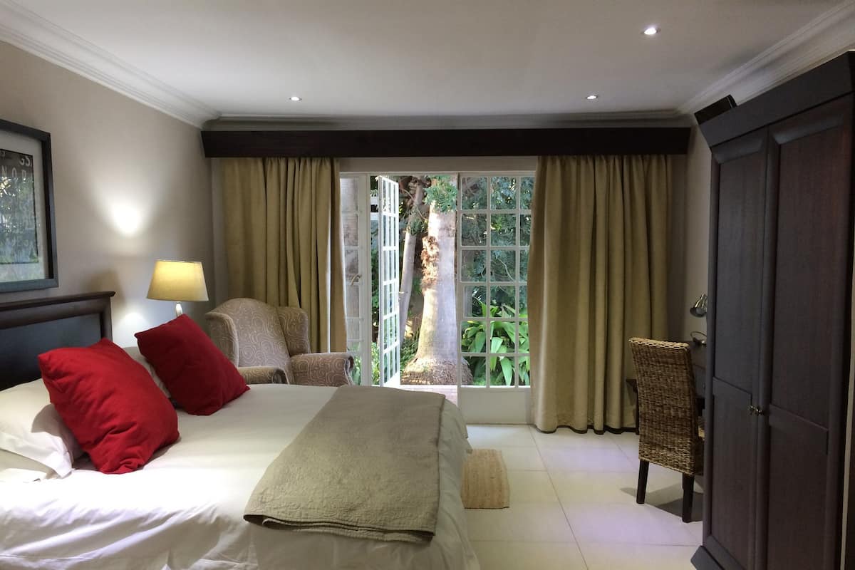 A hotel room with a bed, a chair, a lamp, and a view of greenery through the window.