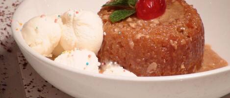 Un dessert composto da un budino al caramello guarnito con una ciliegia e menta, accompagnato da palline di gelato alla vaniglia e zuccherini colorati.