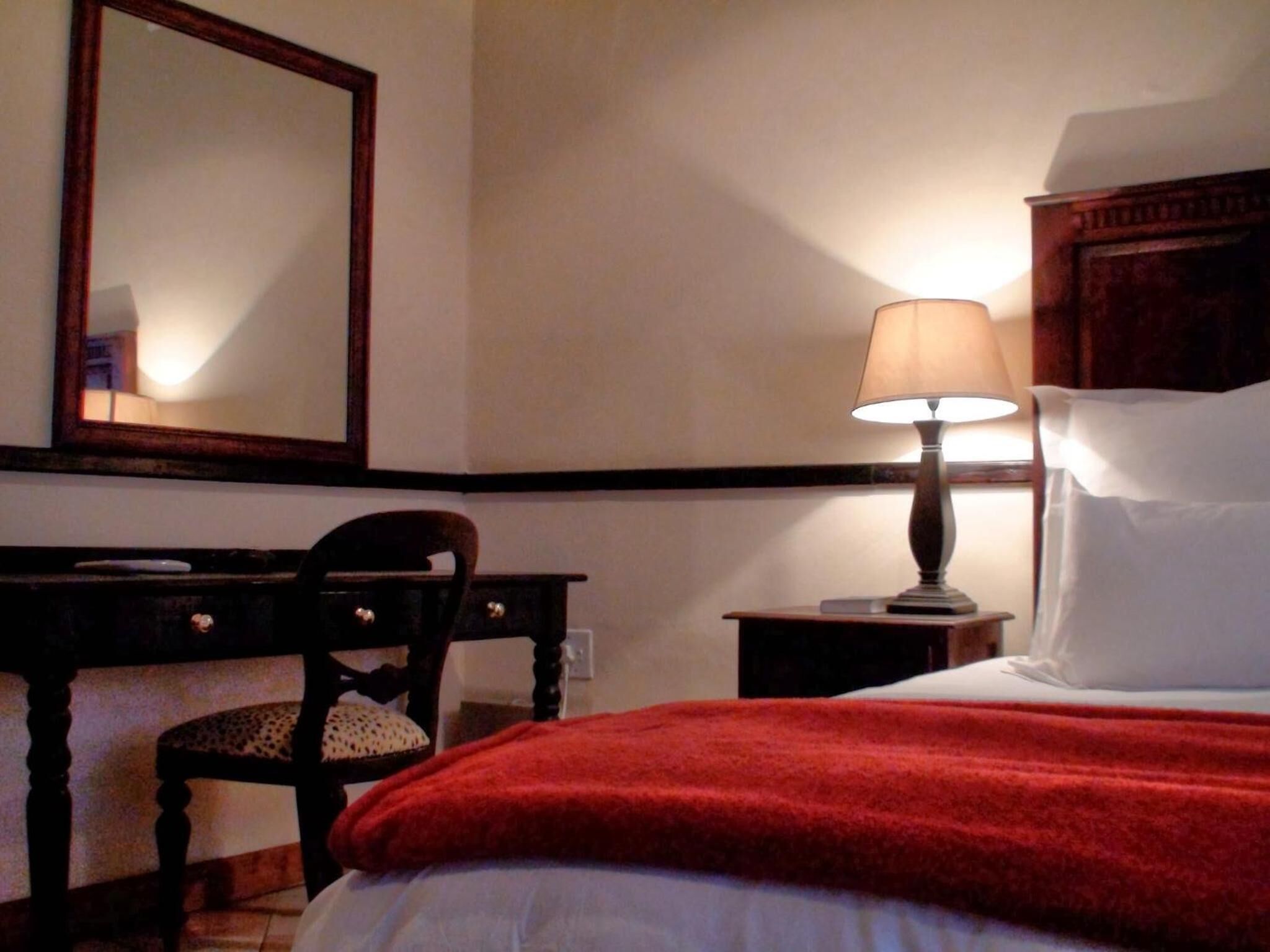 Una habitación de hotel con una cama, una mesita de noche con lámpara, una silla de madera y un escritorio con espejo.