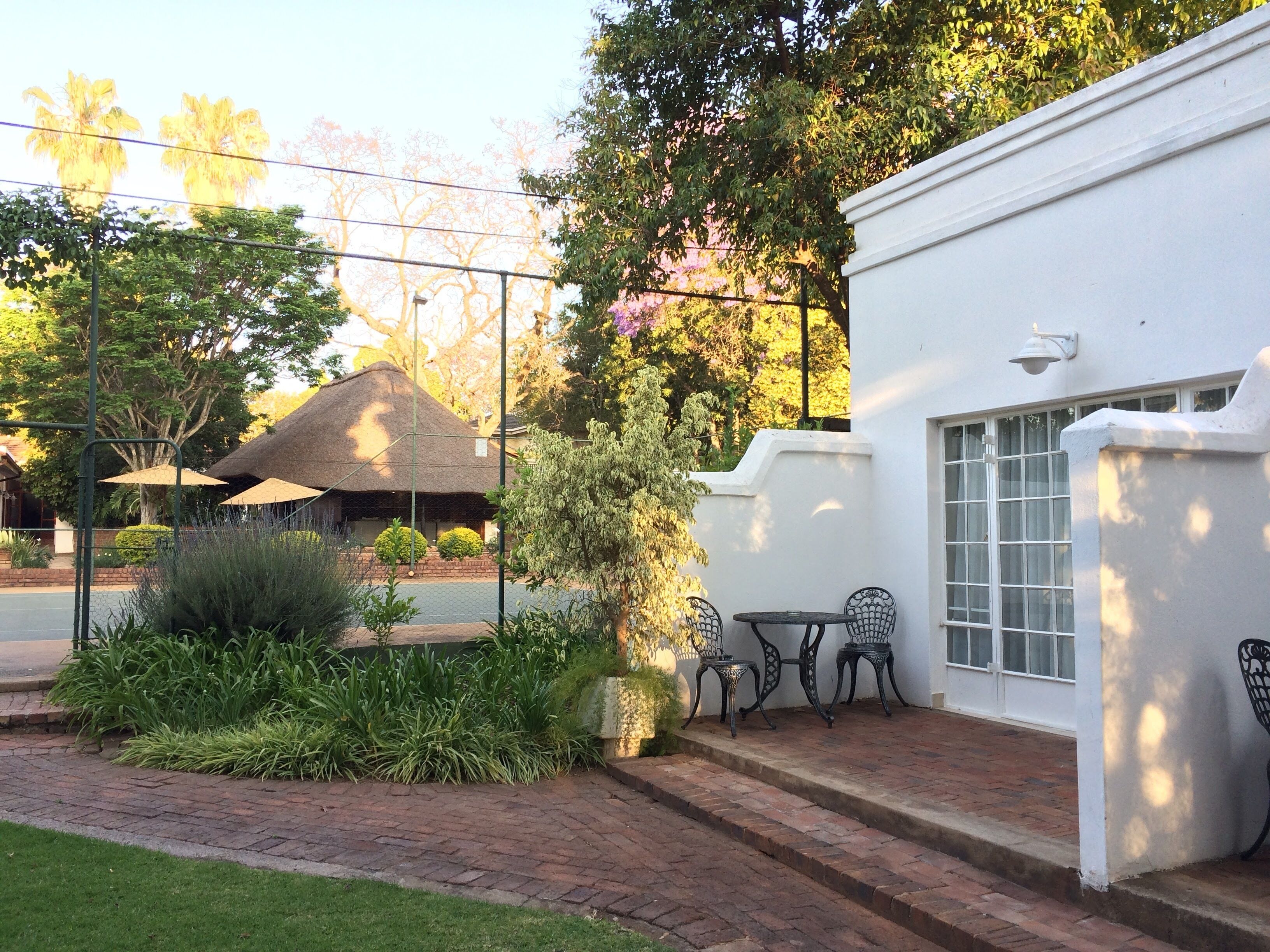A white building with a brick pathway leading to a seating area with metal chairs and a table.