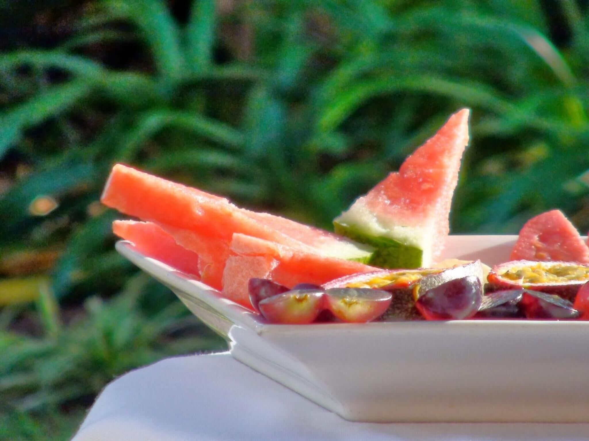 Un plato blanco con rebanadas de sandía y mitades de fruta de la pasión sobre un mantel blanco.