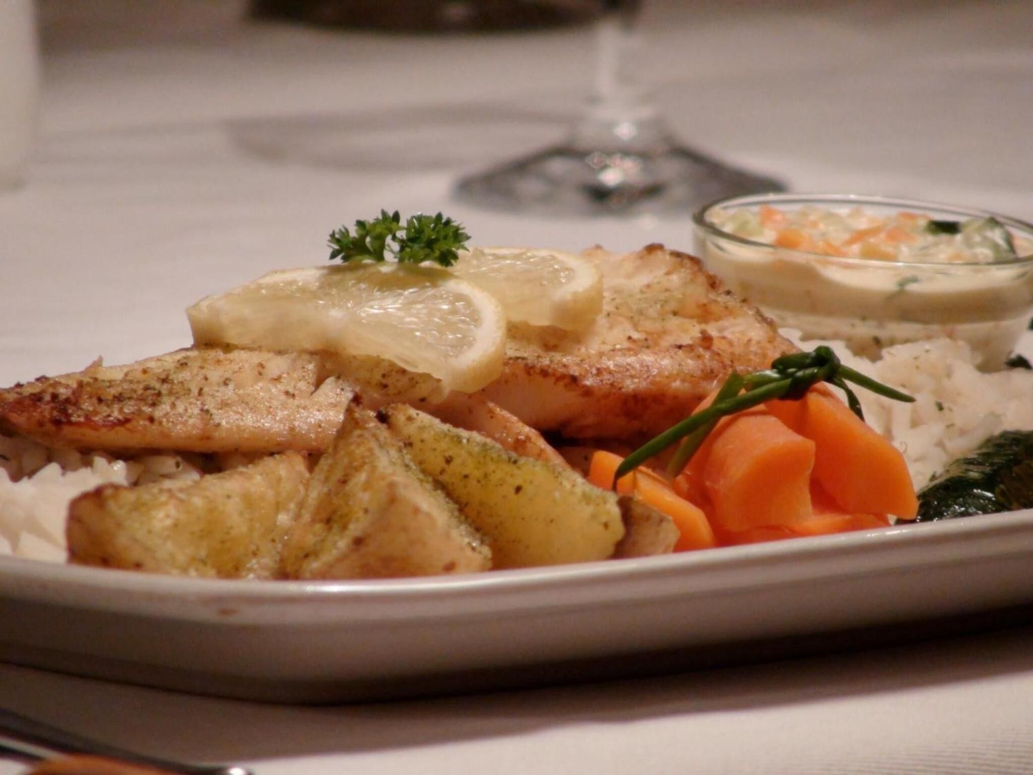 En tallerken mad med ris, kartofler, gulerødder og et stykke fisk, serveret med en lille skål sauce.