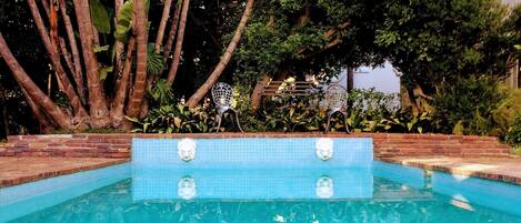 A swimming pool with a tiled edge, surrounded by trees and plants.